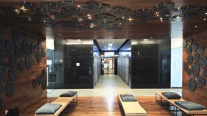 A modern hotel lobby with wooden flooring, a central seating area with benches, and a decorative ceiling.