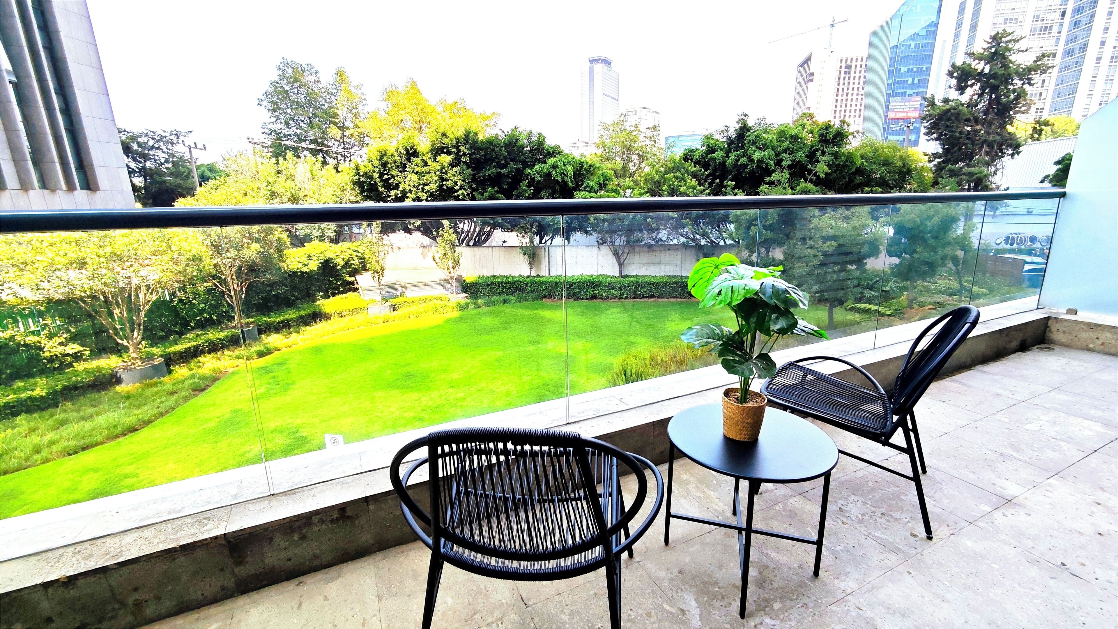 A balcony with two chairs and a potted plant, overlooking a well-maintained lawn and trees.
