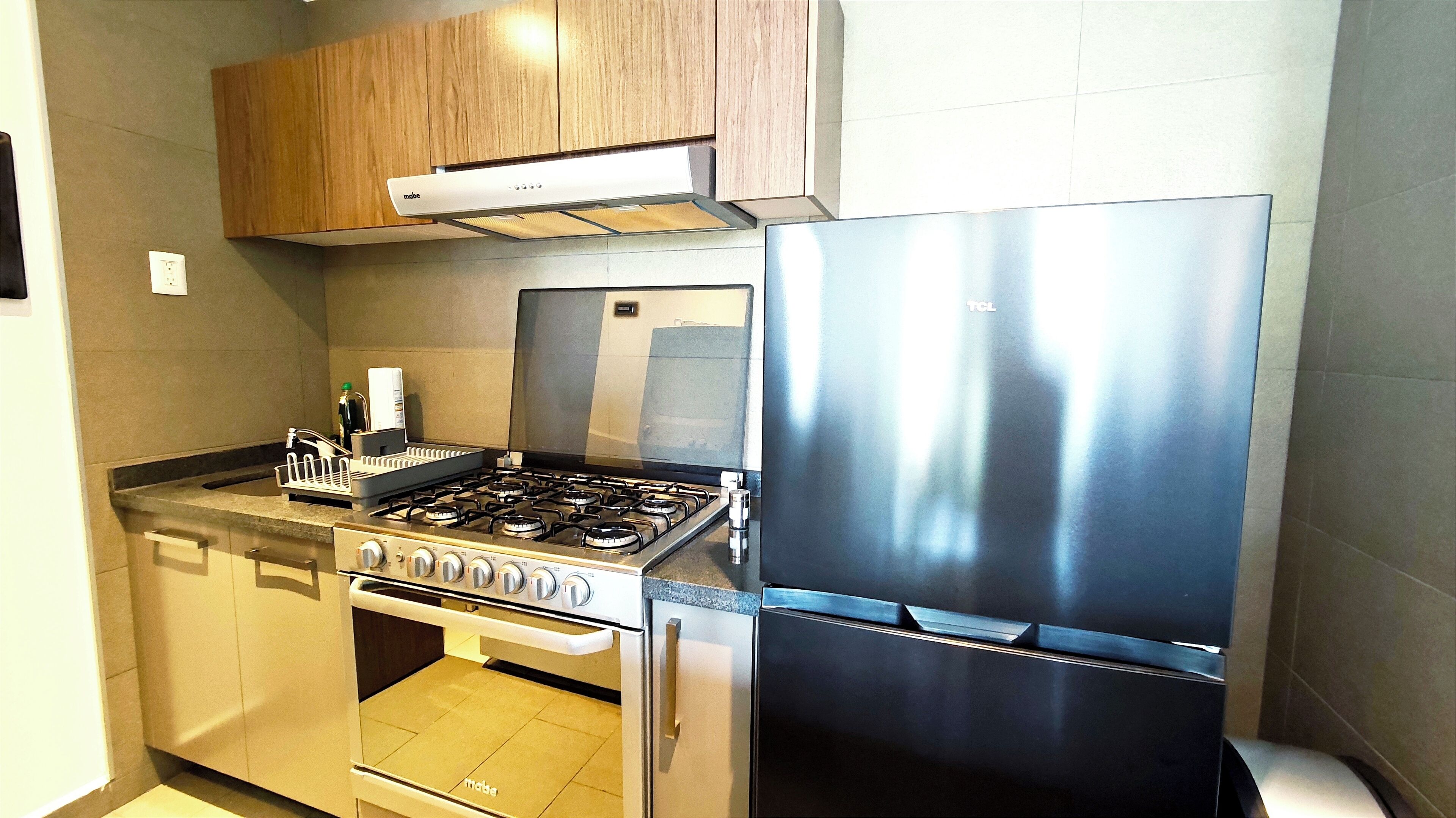 Una cocina moderna con estufa, horno y refrigerador de acero inoxidable, gabinetes de madera y salpicadero de azulejos.