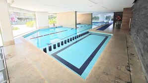 A swimming pool with clear lanes, a lifebuoy, and a view of greenery outside.