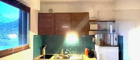 Cocina compacta con pileta, estufa y microondas. Se aprecia una ventana que ofrece vistas de un paisaje montañoso.