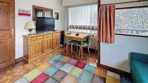 Una habitación pequeña y acogedora con un armario de madera, un televisor, una mesa de comedor con sillas y una alfombra colorida.