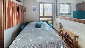 Un dormitorio con una cama, una ventana, un radiador y un banco de madera.