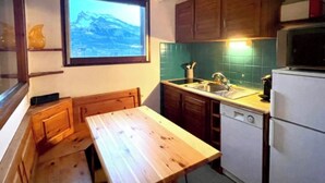 Una cocina compacta con armarios de madera, un banco integrado, una ventana con vistas a la montaña y un refrigerador pequeño.