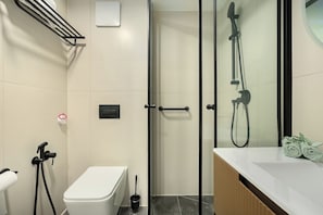 A modern bathroom with a glass shower enclosure, a toilet, and a sink with a towel on the counter.