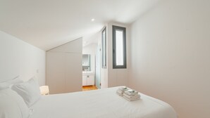 Quarto com uma cama, uma janela e um banheiro visível ao fundo.