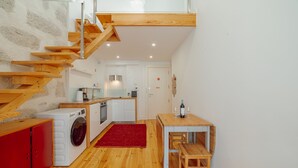 Uma cozinha compacta com máquina de lavar, área de refeições com mesa e banco, e escada de madeira.