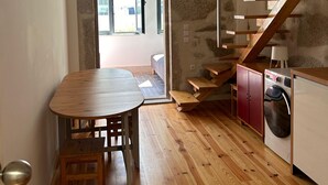 Uma cozinha compacta com uma mesa e banco de madeira, uma máquina de lavar e uma escada que leva a um andar superior.