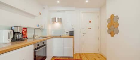 A compact kitchen with a coffee maker, microwave, and oven, a wooden countertop, and a red rug.
