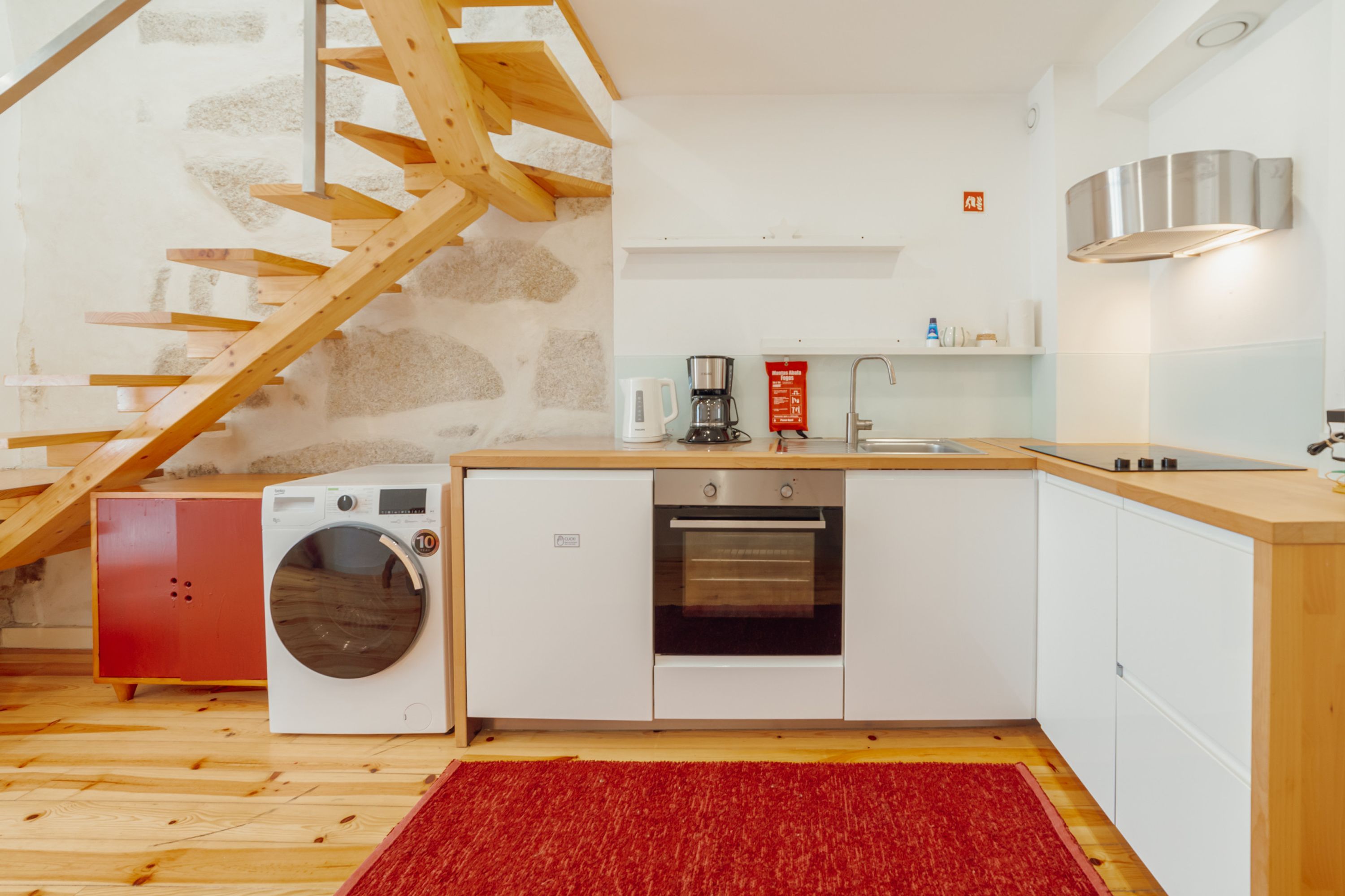 A compact kitchen with a washing machine, oven, and wooden staircase.