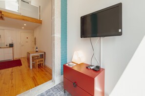 A modern hotel room with a flat-screen TV mounted on the wall, a wooden desk with a chair, a red dresser, and a small table with a lamp. - Marques 1243 Mezzanine by Vacationy (Porto)