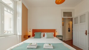 Habitación de hotel con una cama grande, paredes blancas, un cabecero naranja y vistas al exterior.