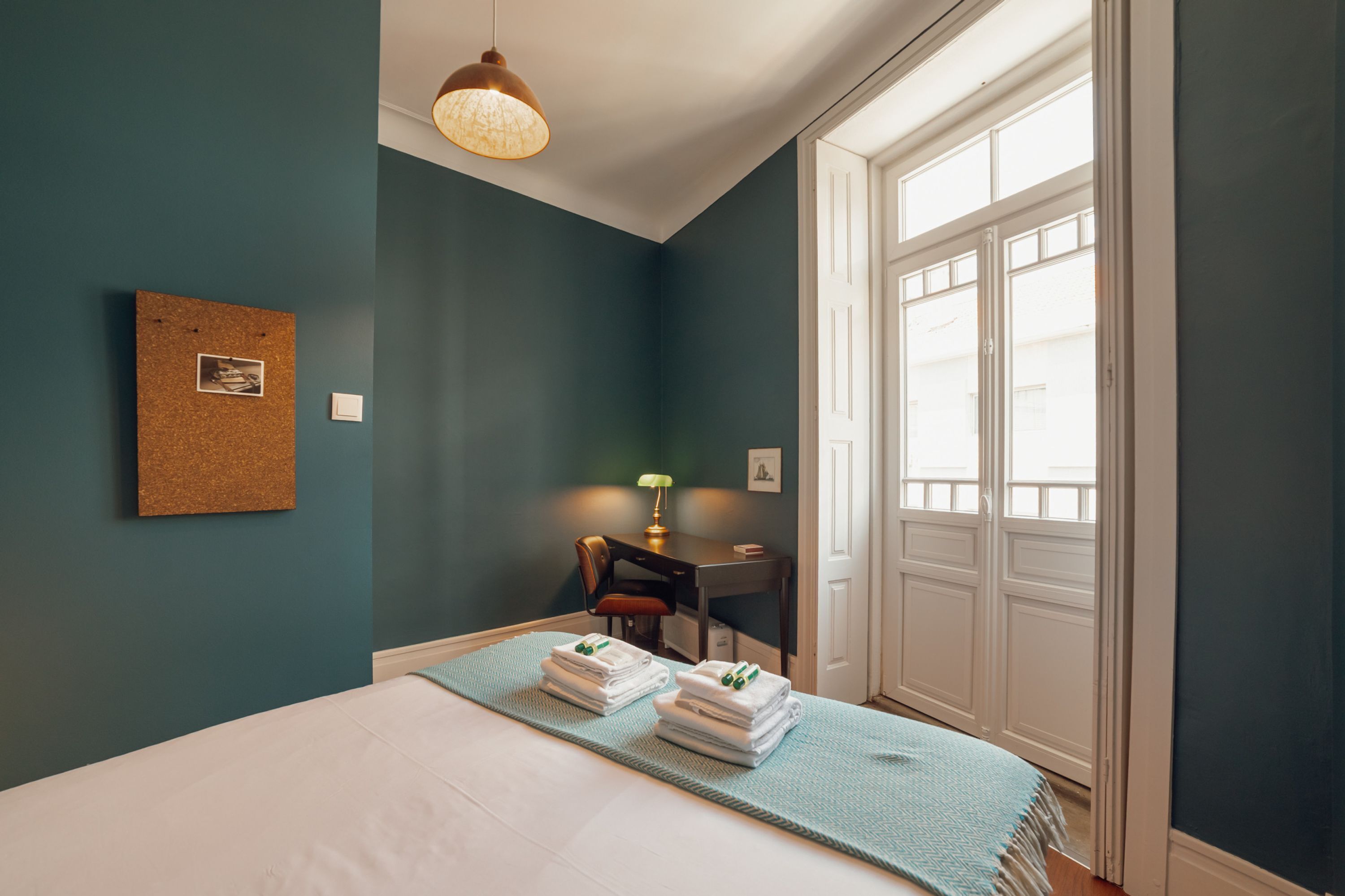 A bedroom with a bed, a desk, a chair, and a window.