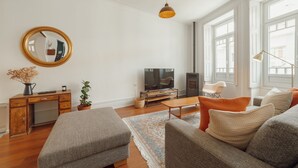 Una sala de estar con un escritorio de madera, un televisor, un sofá y un amplio ventanal.