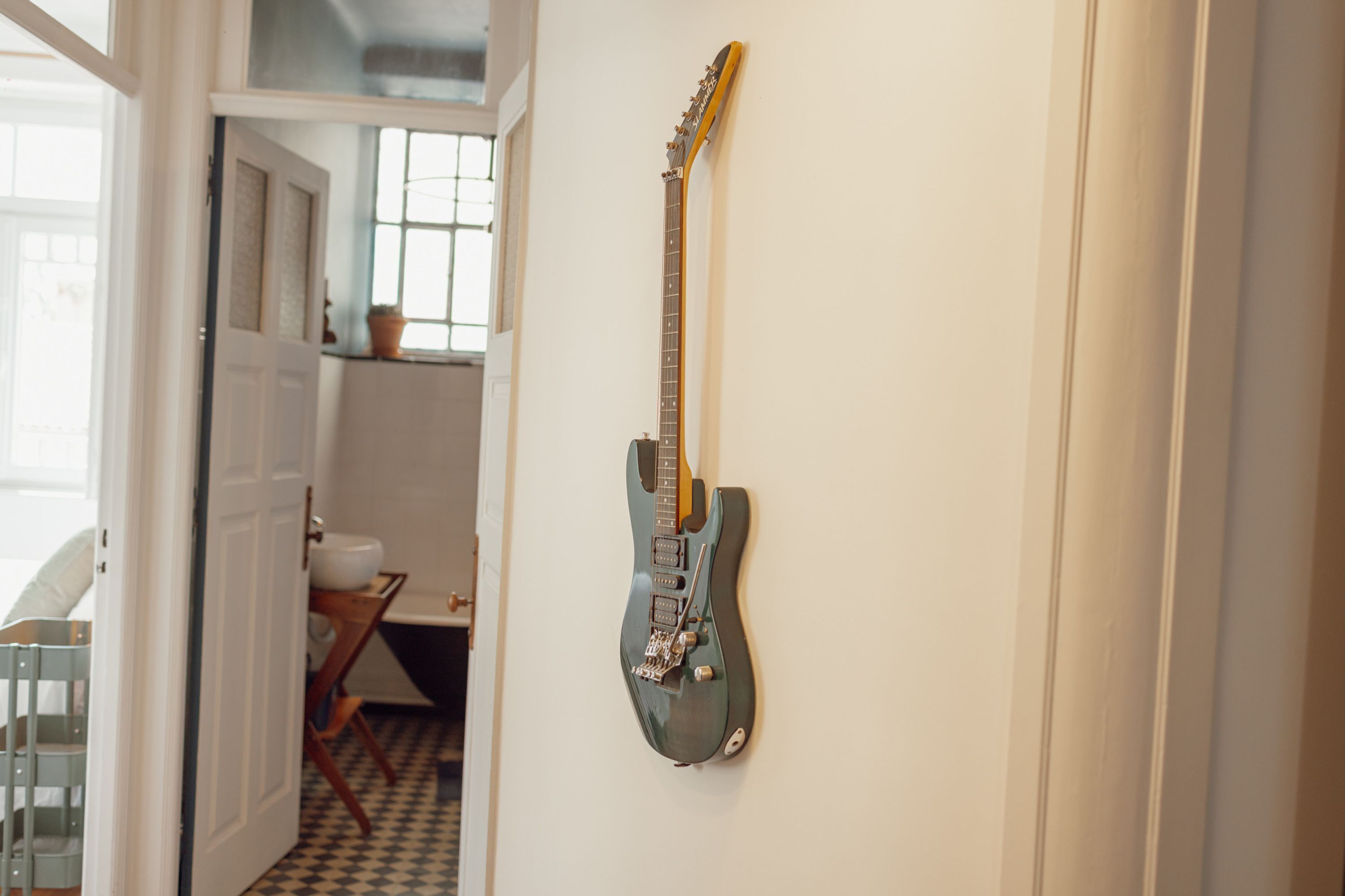 A room with a guitar hanging on the wall, a door leading to another room, and a window with a view.