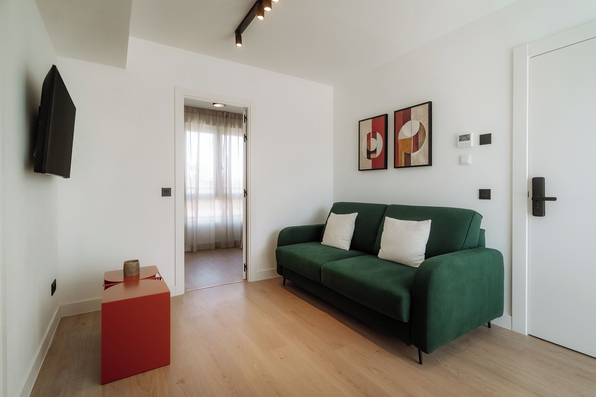 Una sala de estar moderna con un sofá verde, una mesita auxiliar roja y un televisor de pantalla plana montado en la pared.