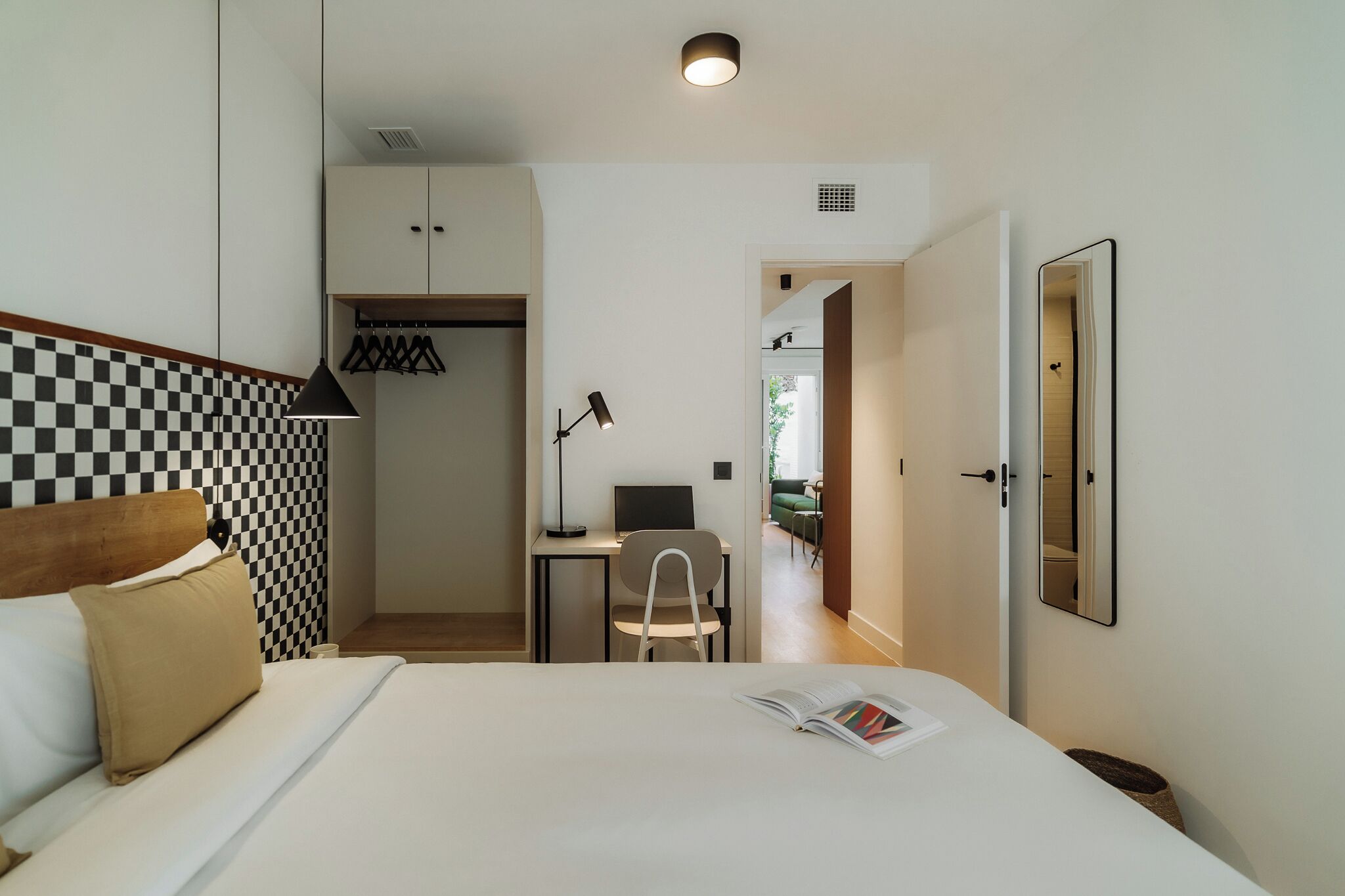 Una habitación de hotel con cama, escritorio, silla, armario y espejo.