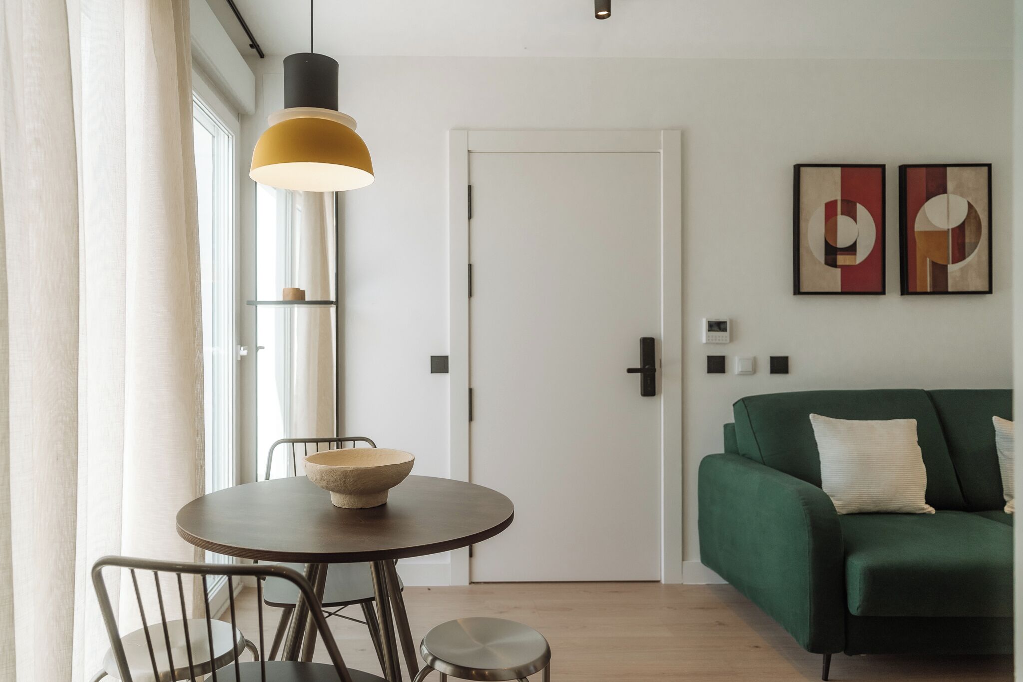 Una sala de estar moderna con una mesa de comedor redonda, un sofá verde y arte abstracto en la pared.