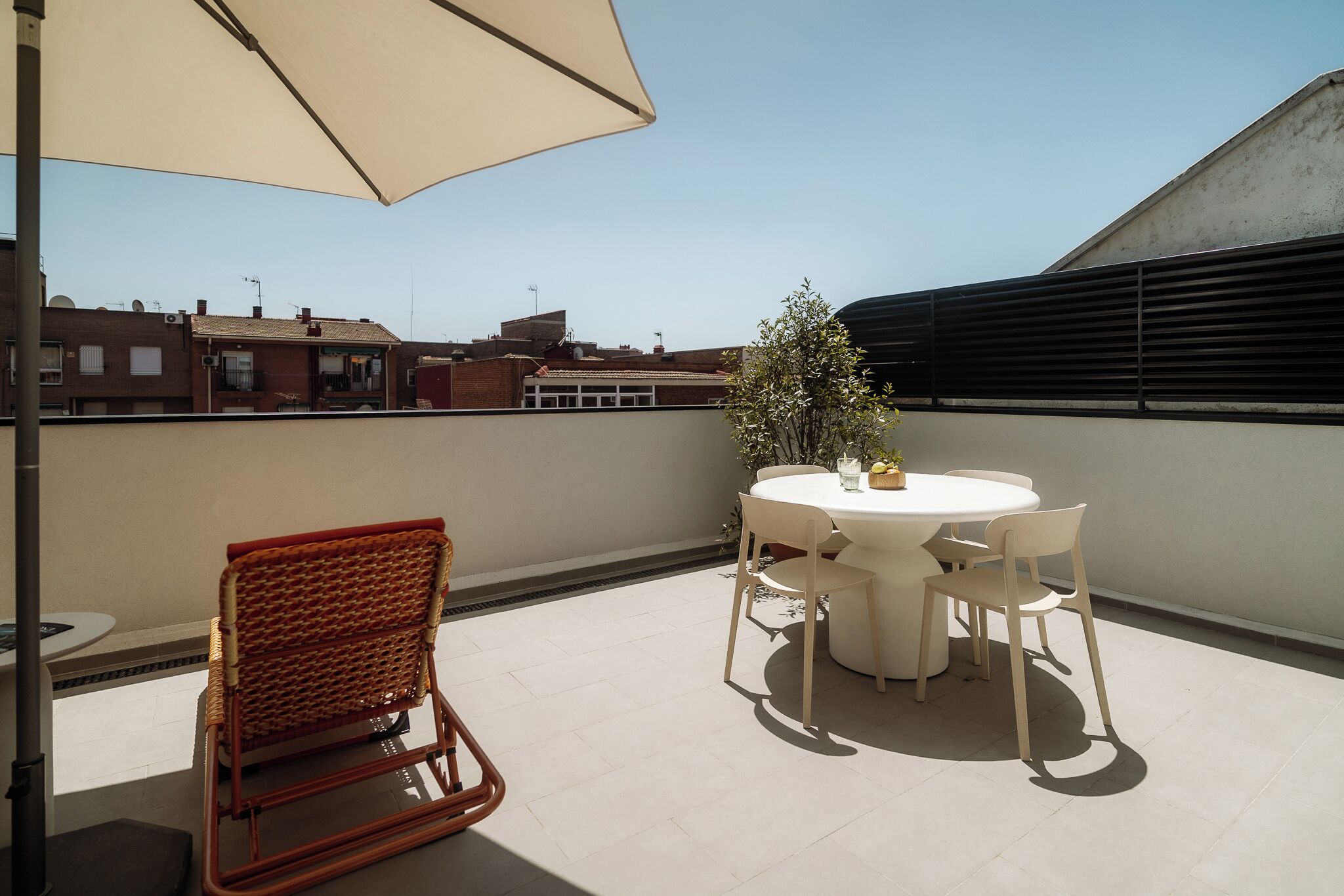 Una terrazza sul tetto con un tavolo rotondo e sedie, una sedia in vimini e un ombrellone grande.