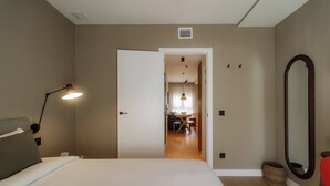 A hotel room with a bed, bedside lamp, and a mirror. There is a door leading to a dining area with a table and chairs. - Via Monte Apartments by Olala Homes (Madrid)
