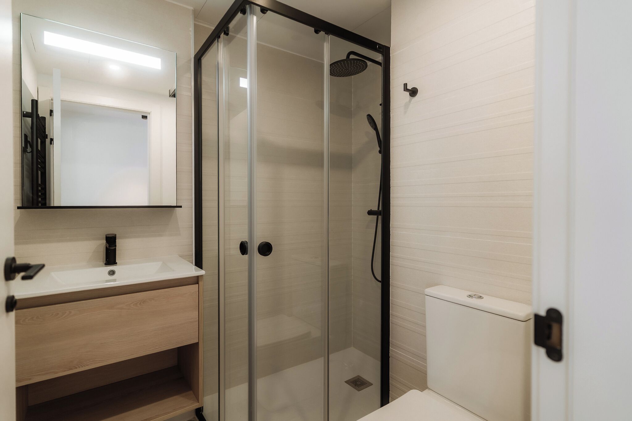 Een moderne badkamer met een glazen douchecabine, een wit wastafeltje en een toilet.