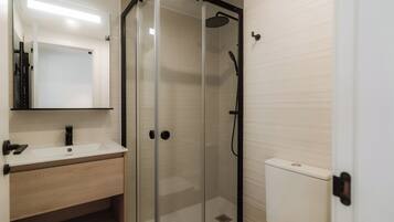 Een moderne badkamer met een glazen douchecabine, een wit wastafeltje en een toilet.