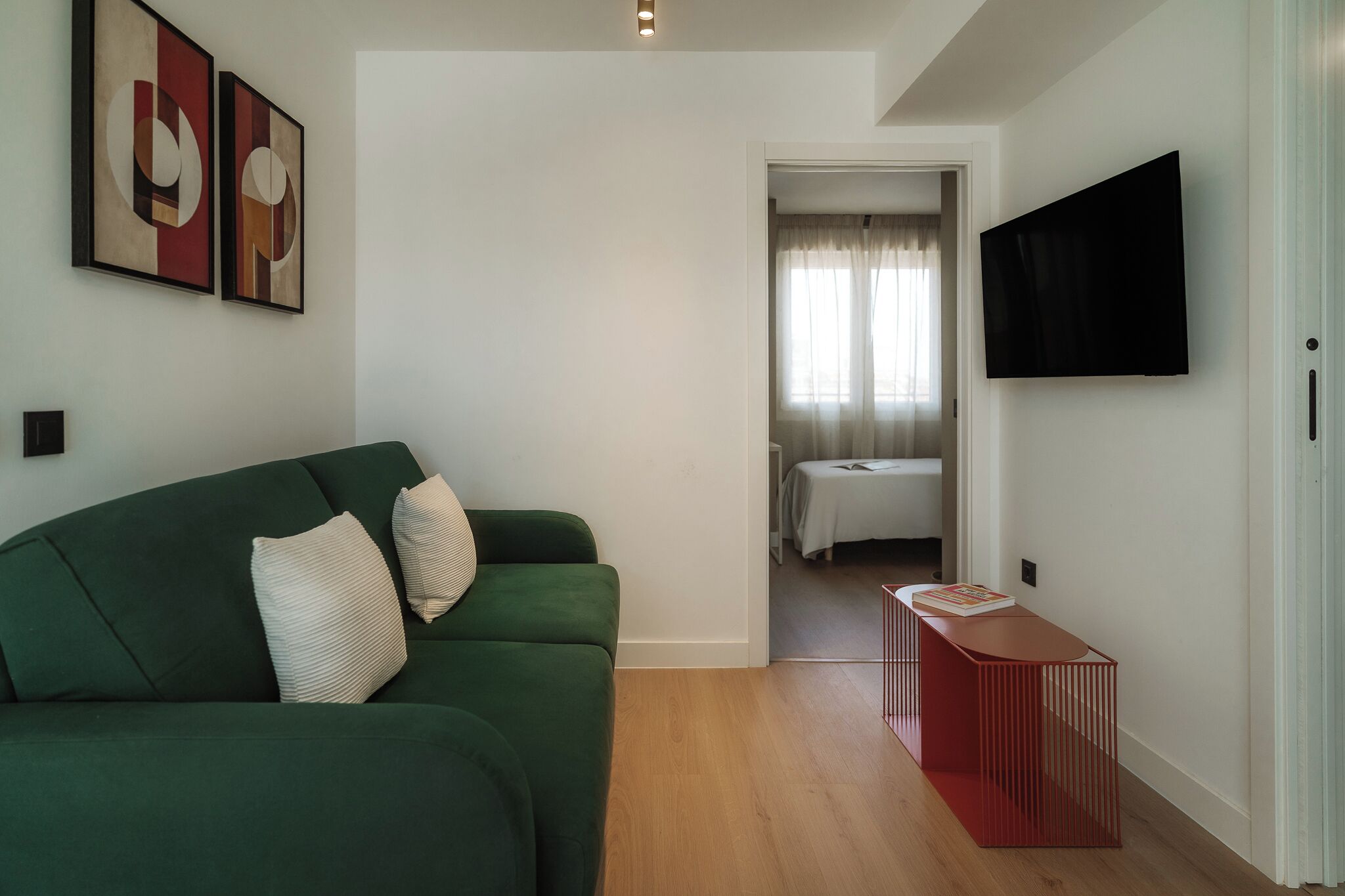 A modern living room with a green sofa, a red side table, and abstract wall art.