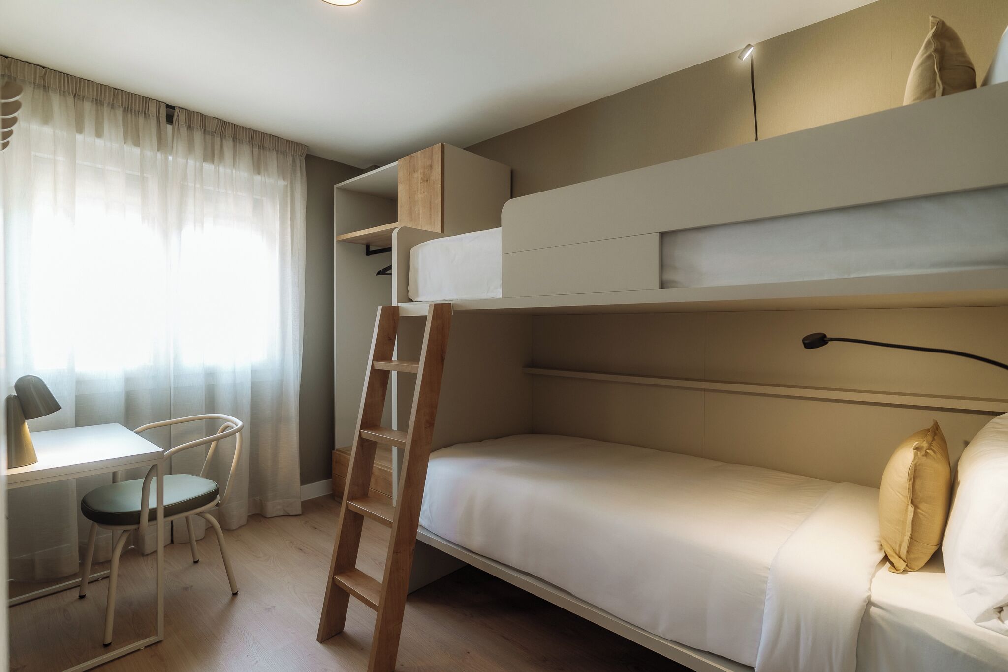 Una habitación pequeña con una cama litera, un escritorio con silla y una escalera.