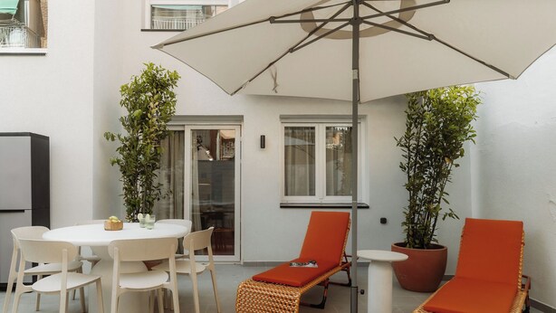 A patio with a round table, chairs, two lounge chairs, a large umbrella, and potted plants. - Via Monte Apartments by Olala Homes (Madrid)