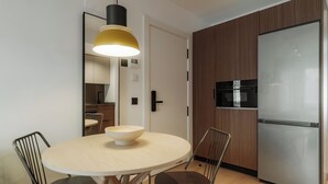 A modern kitchen with a round dining table, two chairs, a large pendant light, and a built-in refrigerator. - Via Monte Apartments by Olala Homes (Madrid)