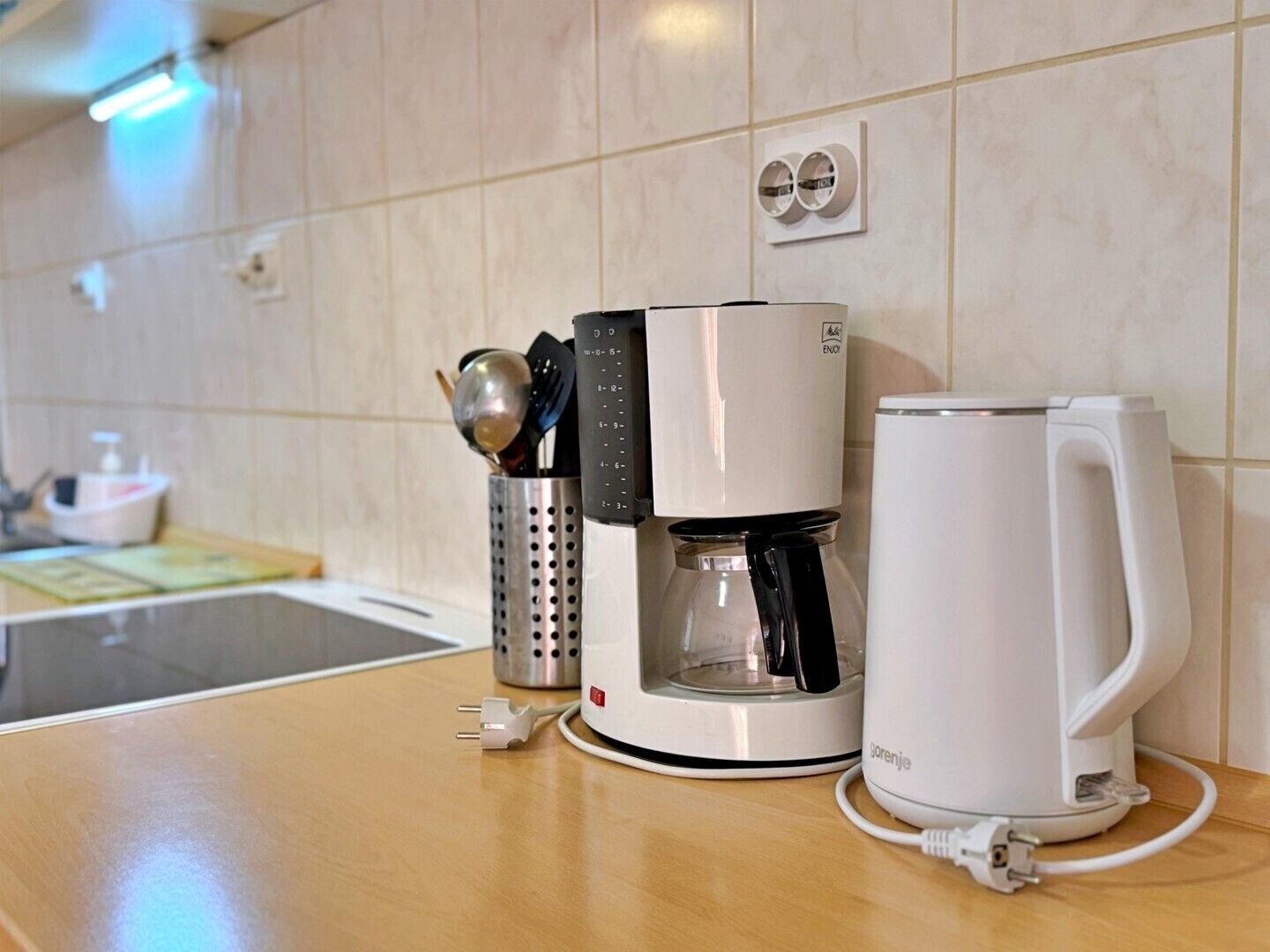 Une machine à café, une tasse et un porte-ustensiles sur un plan de travail de cuisine.