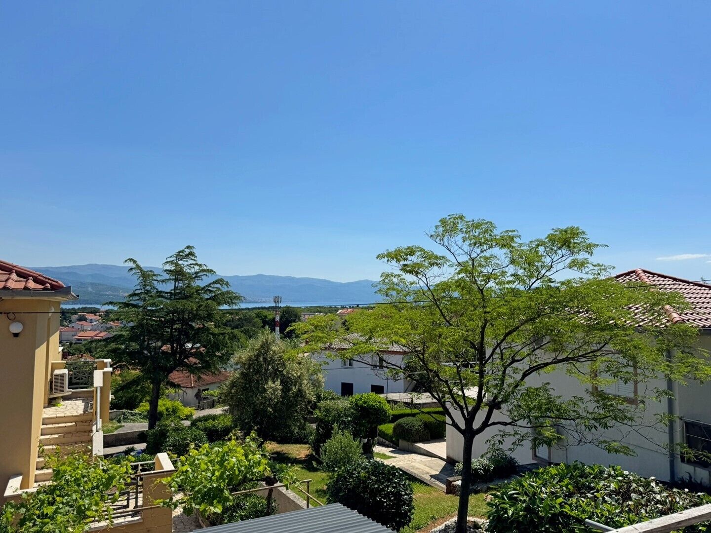 A residential area with a clear view of mountains in the distance, surrounded by greenery and buildings with red-tiled roofs.