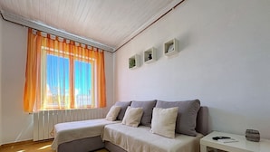 A cozy room with a sofa bed, a small table, and a window with orange curtains. - Apartment Andjelka - with sea view, spacious terrace, two bedrooms, washing machine, pet-friendly, private parking (Šilo)