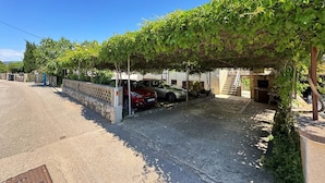 A covered parking area with a stone wall, a red car, and a stone building with a staircase. - Apartment Andjelka - with sea view, spacious terrace, two bedrooms, washing machine, pet-friendly, private parking (Šilo)