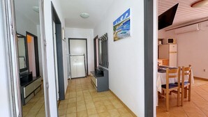 A hallway with a tiled floor, a door, a refrigerator, a painting, and a dining area with chairs and a table. - Apartment Andjelka - with sea view, spacious terrace, two bedrooms, washing machine, pet-friendly, private parking (Šilo)