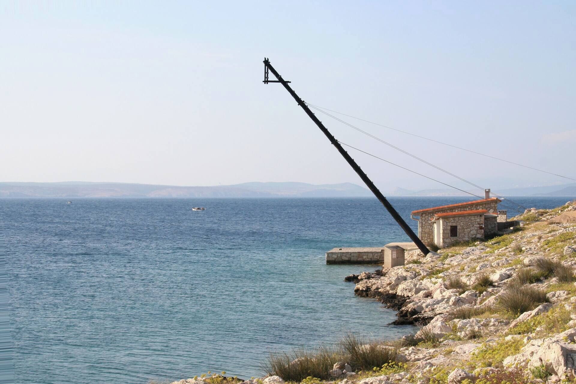 A coastal scene with a stone building and a fishing pole extending over the water.