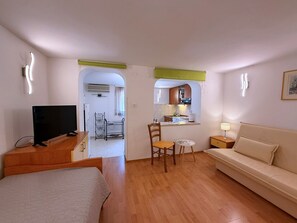 Habitación de hotel compacta con cama, televisión, sofá, una pequeña mesa de comedor y kitchenette.