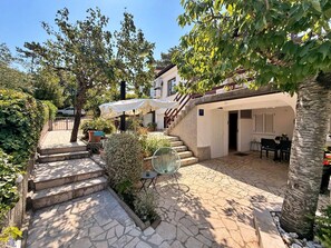 Un patio con suelo de piedra, una escalera, mobiliario exterior y la entrada a un edificio.