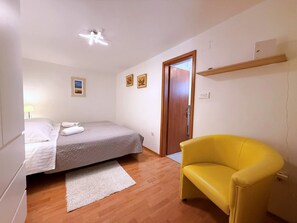 A bedroom with a bed, a chair, a door, and a ceiling fan.