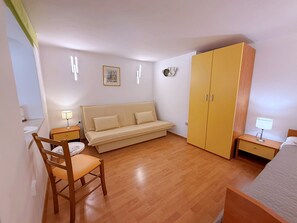 Un dormitorio con sofá cama, una silla de madera, un armario y una mesita de noche con lámpara.