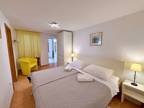 Una habitación de hotel con una cama, lámparas de noche, una silla y una puerta que da a otra habitación.