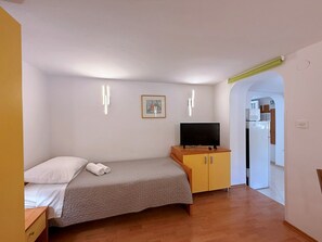 A bedroom with a bed, a television on a wooden cabinet, and a painting on the wall.