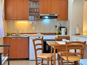 Una cocina compacta con armarios de madera, horno integrado, lavavajillas y una mesa de comedor con sillas.