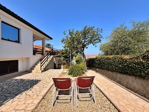 A patio area with a stone floor, two red chairs, and a staircase leading to a building.