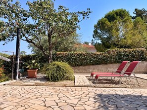 Un patio con suelo de piedra, un conjunto de asientos y un seto al fondo.
