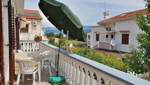 Un balcón con una sombrilla verde, sillas blancas y un tapete verde.