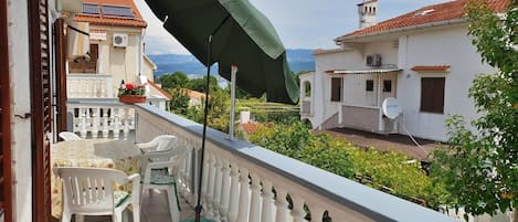 A balcony with a green umbrella, white chairs, and a green mat.