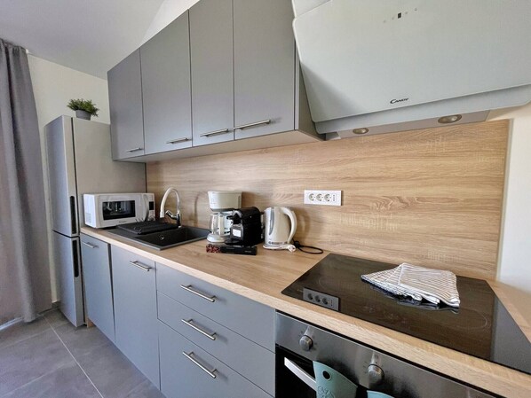 A compact kitchen with grey cabinets, a microwave, a coffee maker, and a kettle.