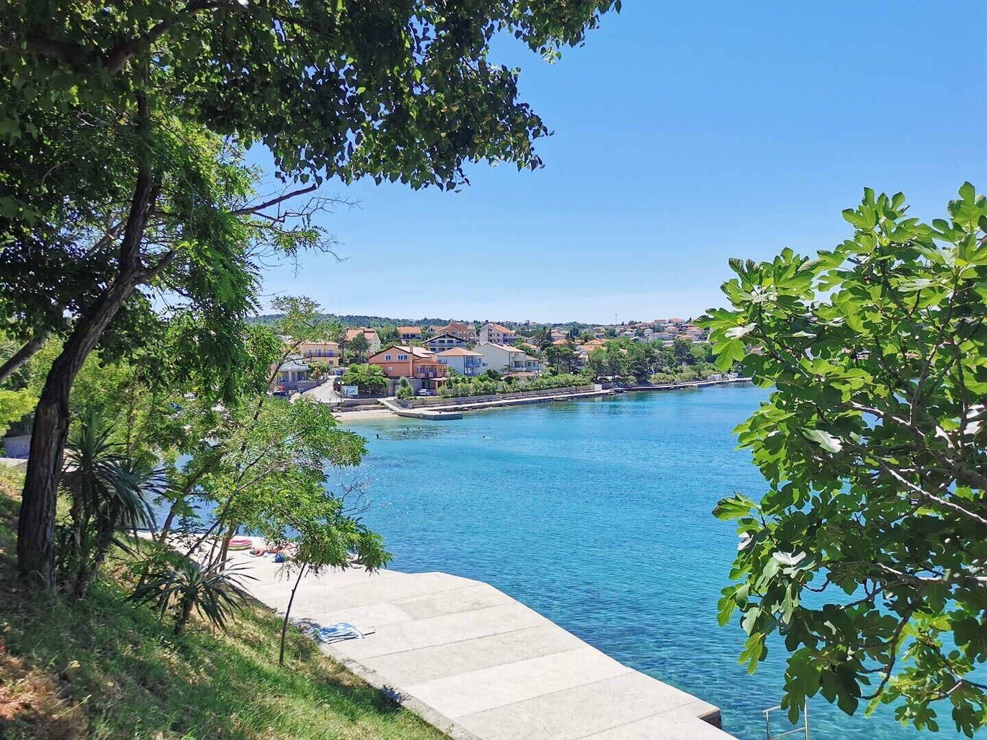 Un pueblo costero con mar azul cristalino, un paseo marítimo y edificios al fondo.