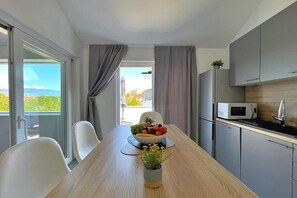 Une cuisine moderne avec une table à manger, des chaises, un saladier de fruits, un four à micro-ondes et une vue sur l’extérieur.